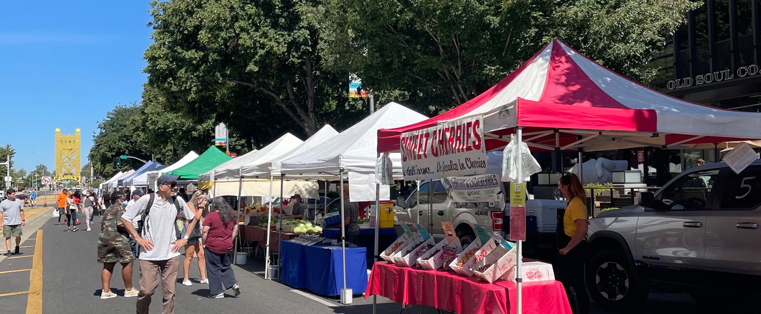 Farmers market in daytime with red, white, and green tents.